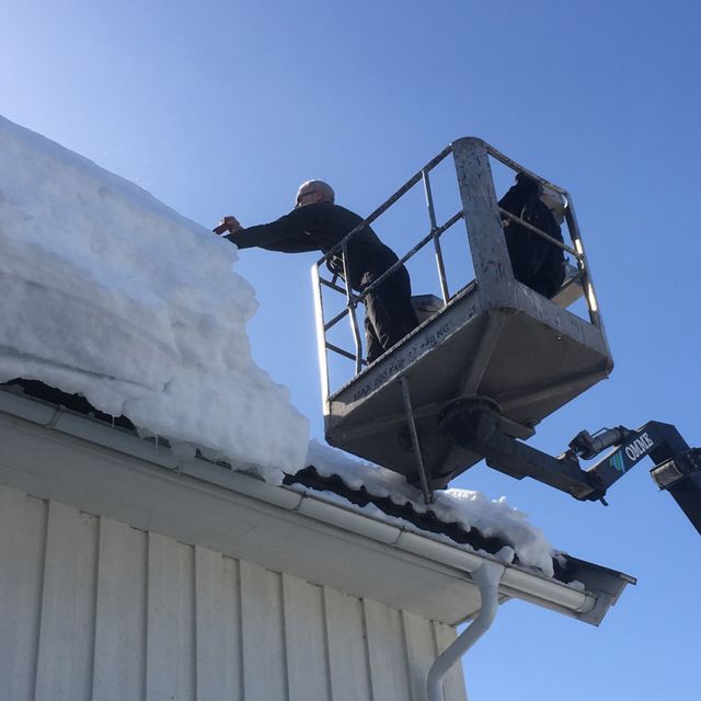 Mann i kran fjerner snø på tak
