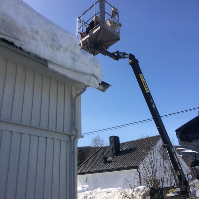 Mann i kran fjerner snø på tak